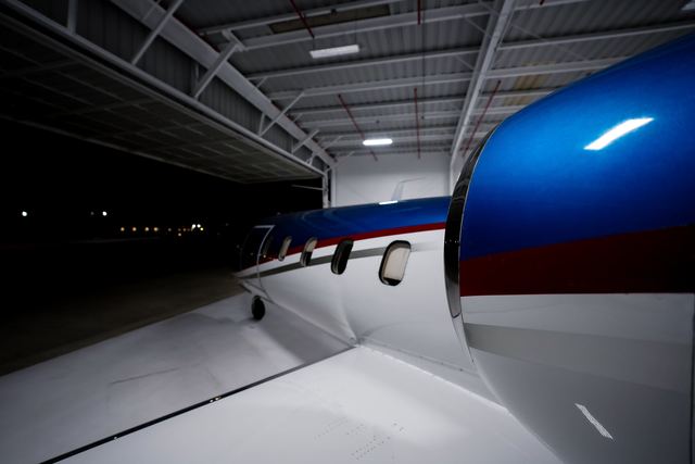 Polished engine inlet lip and blue, red, and white paint on a business jet engine nacelle, in a hangar at night.